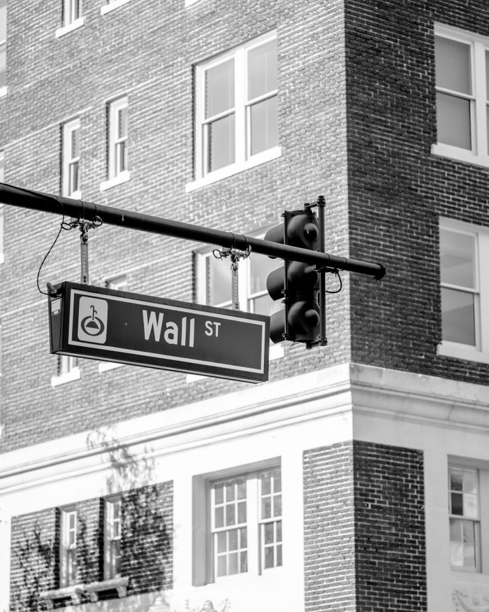 Services Grayscale image of Wall Street sign with traffic lights against a brick building backdrop.